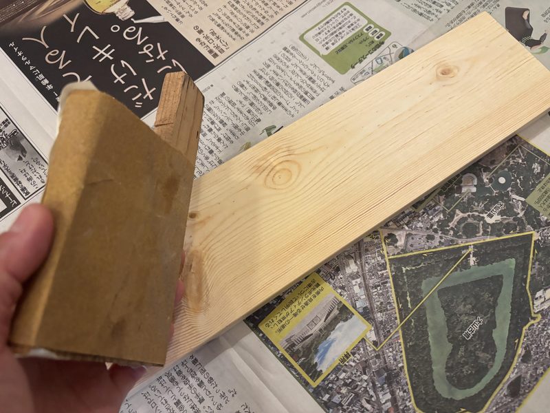 平らな木片に紙やすりを巻きつけて1×4材をやすりがけしているところ