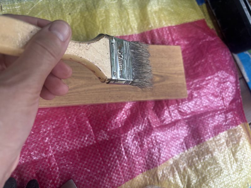 刷毛で1×4材に木部保護塗料を塗っているところ